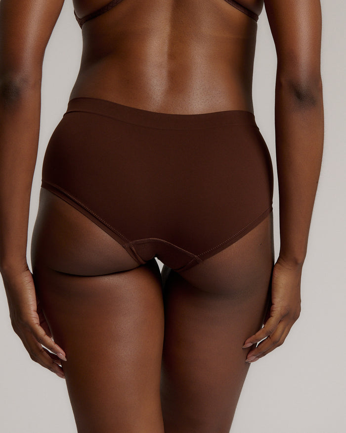 A person wearing a brown mid-rise brief underwear, showing the side profile of the underwear with no visible lines.