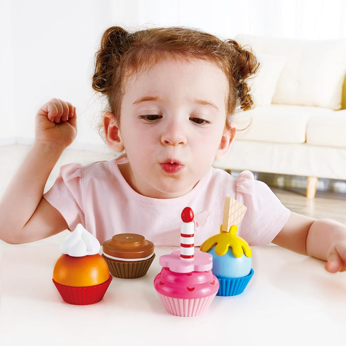 Child playing with colorful toy cupcakes on a white surface