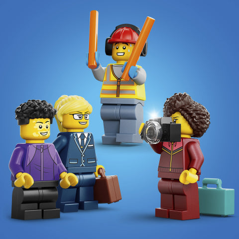 Four LEGO minifigures posed together on a blue studio background: a construction worker holding orange poles, a woman in a purple jacket, a man in a blue suit holding a briefcase, and a woman in a red jacket holding a camera with a teal case beside her.