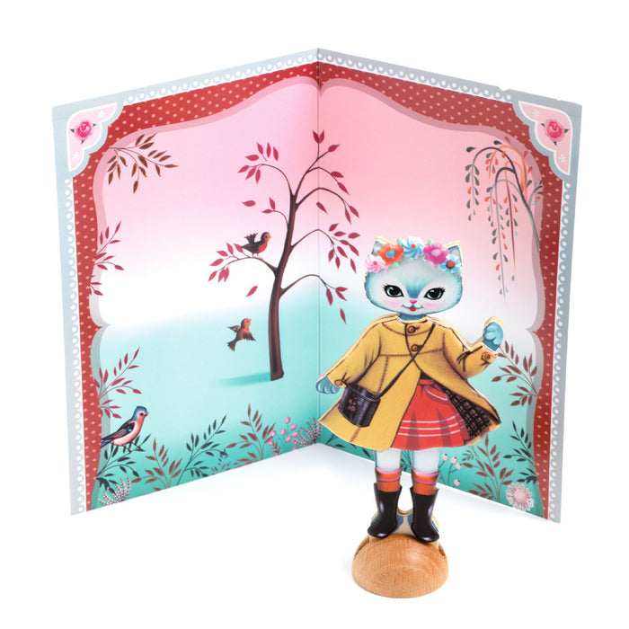 A white dress-up cat wearing a tan coat and red dress standing against a backdrop with a tree and bird on a white background