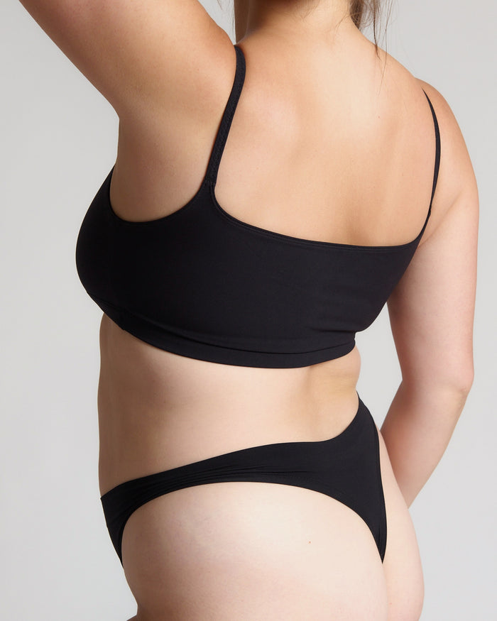 Person wearing a black bra and underwear on a plain background