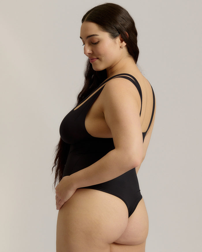 Woman wearing a black bodysuit against a plain background