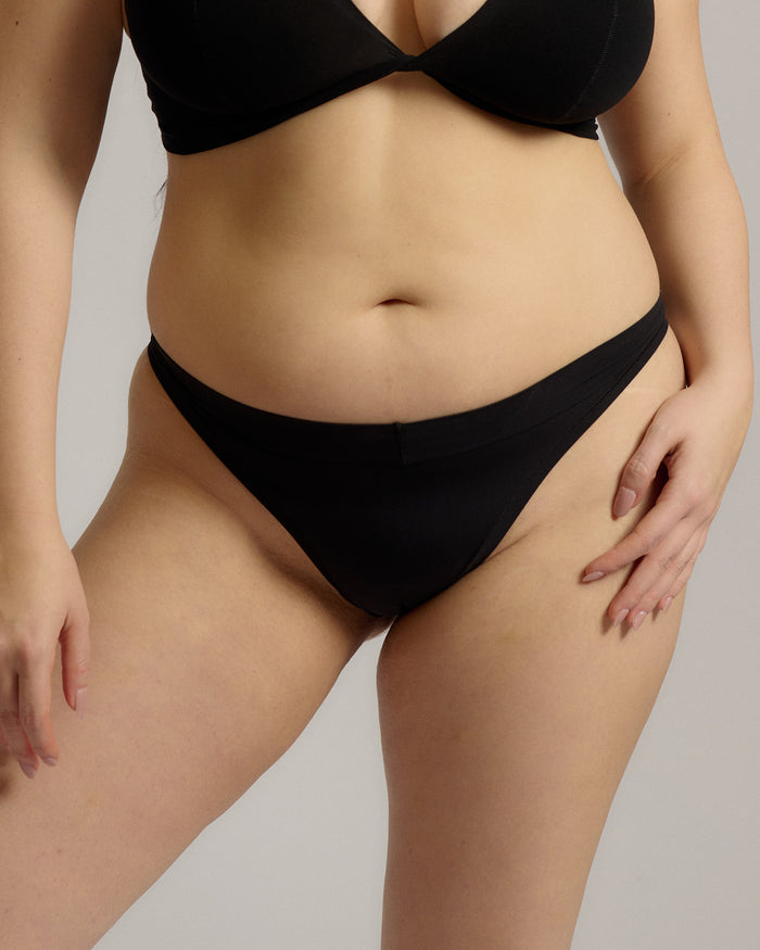 A woman wearing black thong underwear designed with a mid-rise cut.