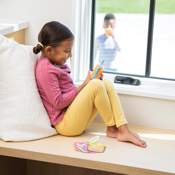 Child sitting on a windowsill reading a book with a view of a car outside.