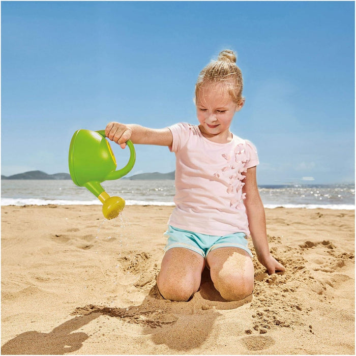 Child playing with a green watering can on the beach