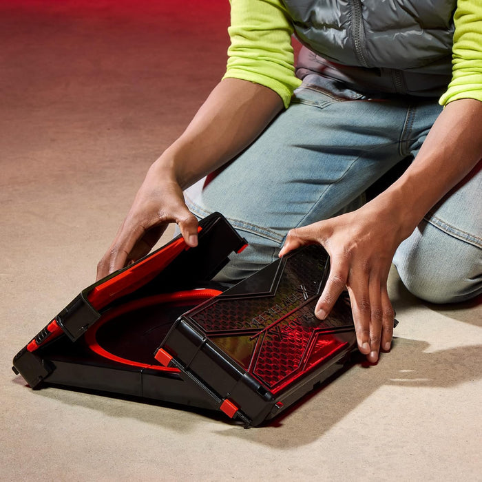 Person assembling a red and black Beystadium on a beige floor.