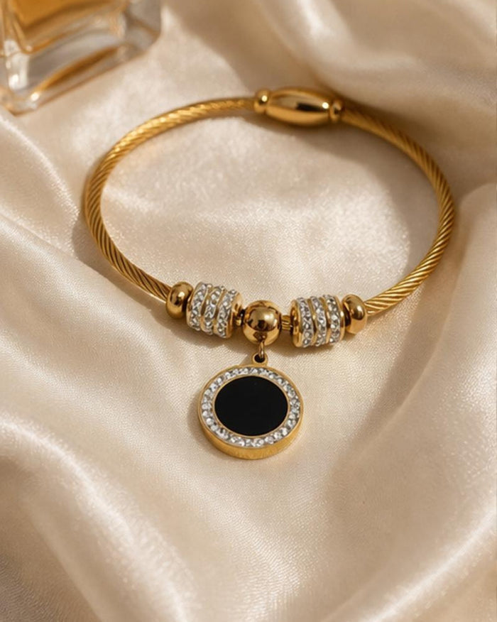 Gold plated stainless steel bangle bracelet with black enamel charm on soft silk fabric close up product view