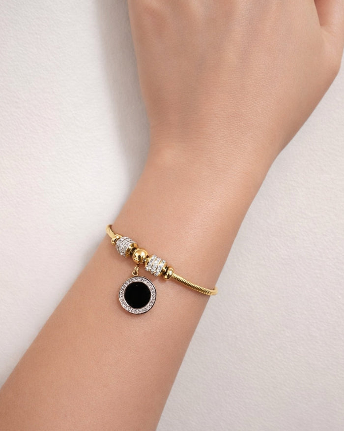 Gold plated stainless steel bangle bracelet with black enamel charm worn on wrist close up lifestyle view