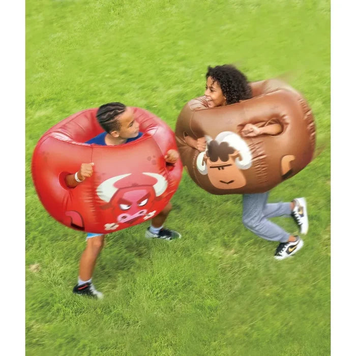 Two kids playing with inflatable bumper balls on a green grass lawn. One ball is red with a white bull graphic, and the other is brown with a ram print.