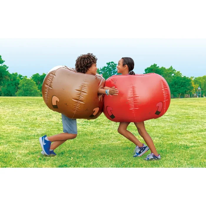 Two children playing inflatable bumper balls on a grassy field, with one child wearing a brown ball and the other wearing a red ball.