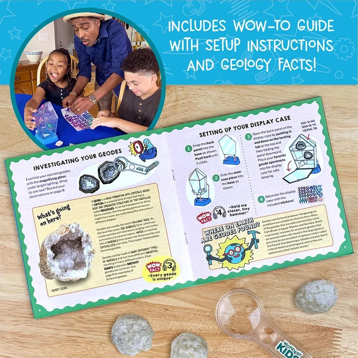An open children's geology kit booklet on a wooden surface, showing instructions and geode facts, with a circular inset photo of a man and two children looking at a geode. The booklet includes a blue header reading 'INCLUDES WOW-TO GUIDE WITH SETUP INSTRUCTIONS AND GEOLOGY FACTS!' and a green border around the pages.