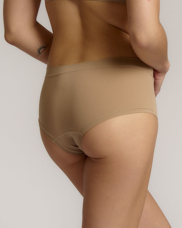 A person wearing a beige mid-rise brief with no visible lines, made from a stretchy fabric, showcasing the design's comfort and fit.