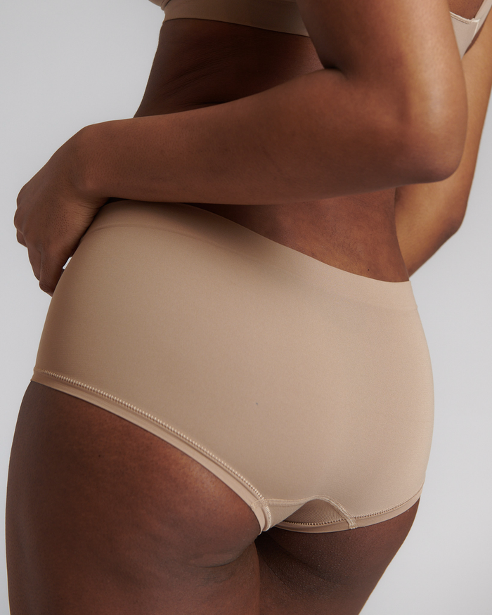 A person wearing a beige mid-rise brief with no visible lines, made from a stretchy fabric.