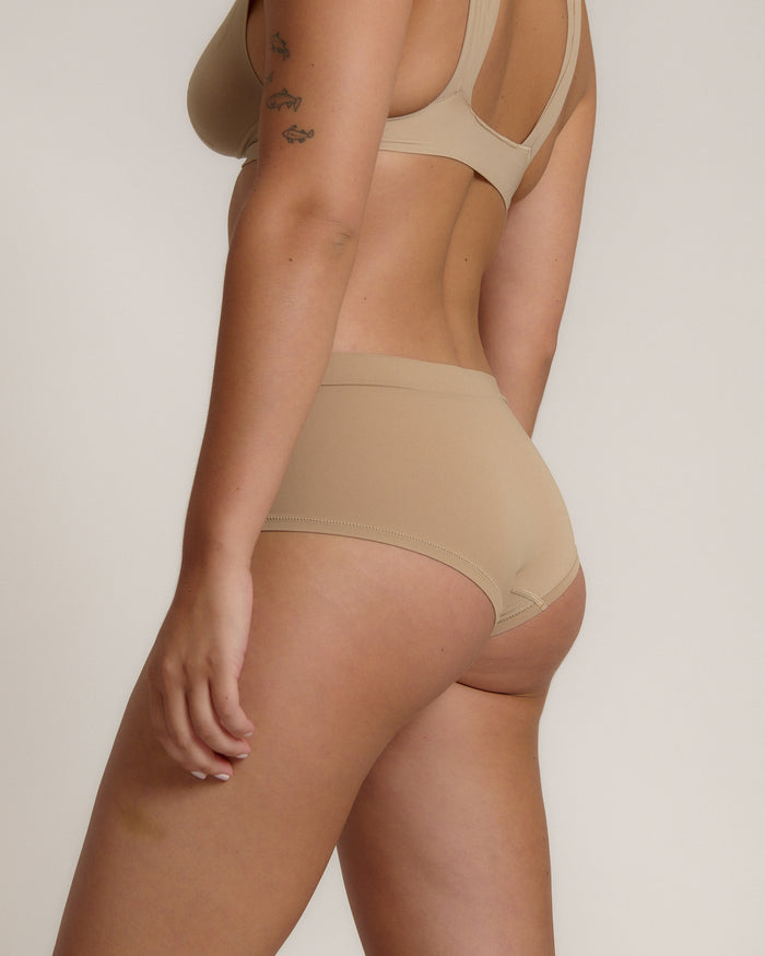 A person wearing a beige mid-rise brief with no visible lines, made from a stretchy fabric, showcasing the design's comfort and fit.