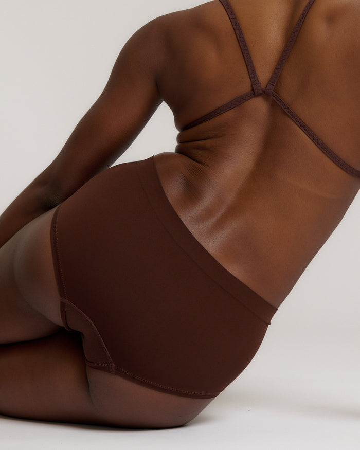 A person wearing a brown mid-rise brief underwear, showing the side profile of the underwear with no visible lines.