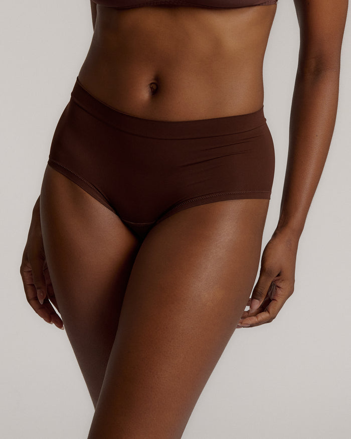 A person wearing a brown mid-rise brief underwear, showing the side profile of the underwear with no visible lines.