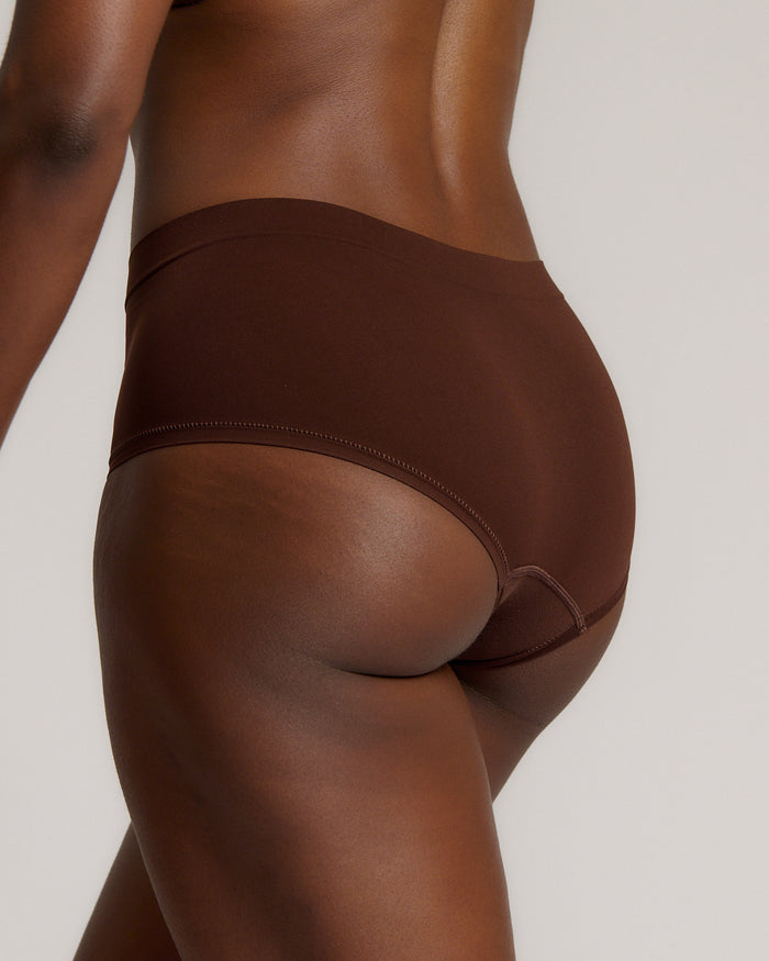 A person wearing a brown mid-rise brief underwear, showing the side profile of the underwear with no visible lines.