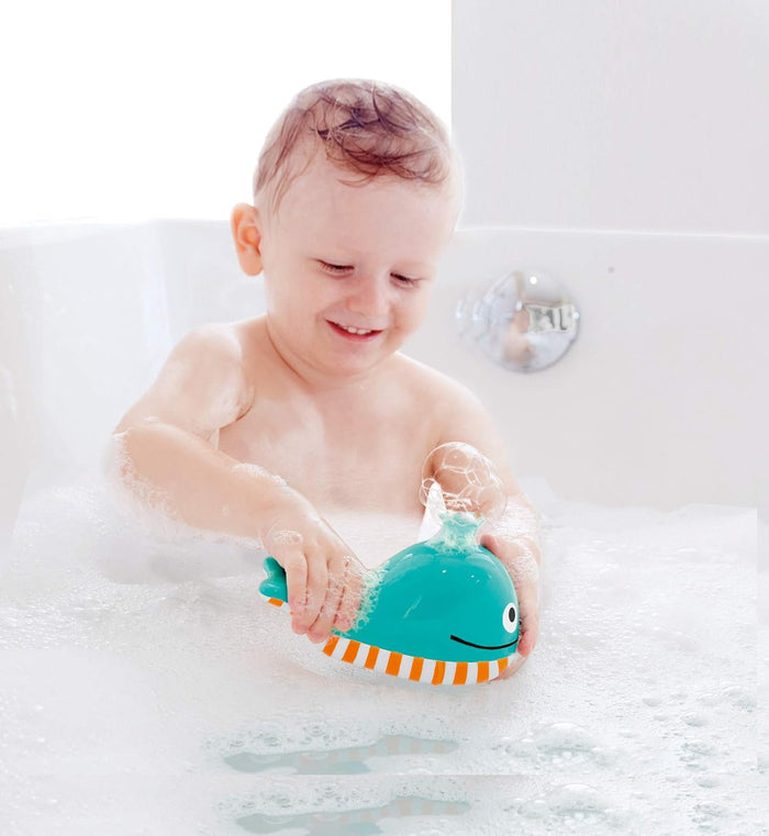 Child playing with a teal bath toy in the shape of a whale in a bathtub filled with bubbles