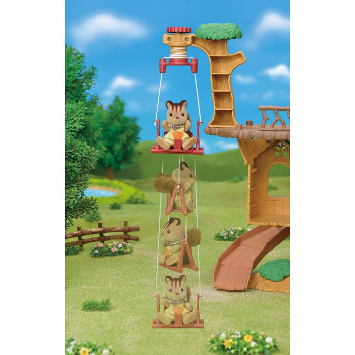 A toy treehouse playset with four hanging squirrel swings suspended from a tree trunk, shown in a landscaped outdoor scene with grass, trees, flowers, and a blue sky backdrop.