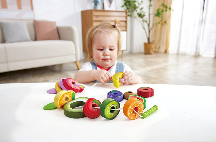 Child playing with the Caterpillar Fruit Feast Set on a white table in a living room.