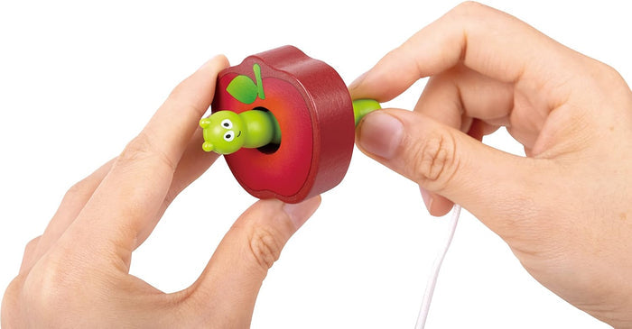 Two hands holding a red wooden apple with a light green caterpillar going through a hole in the center.