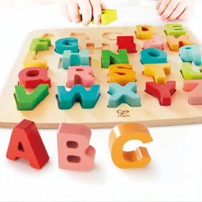 Colorful wooden alphabet puzzle with letters and a hand placing a letter block on it.