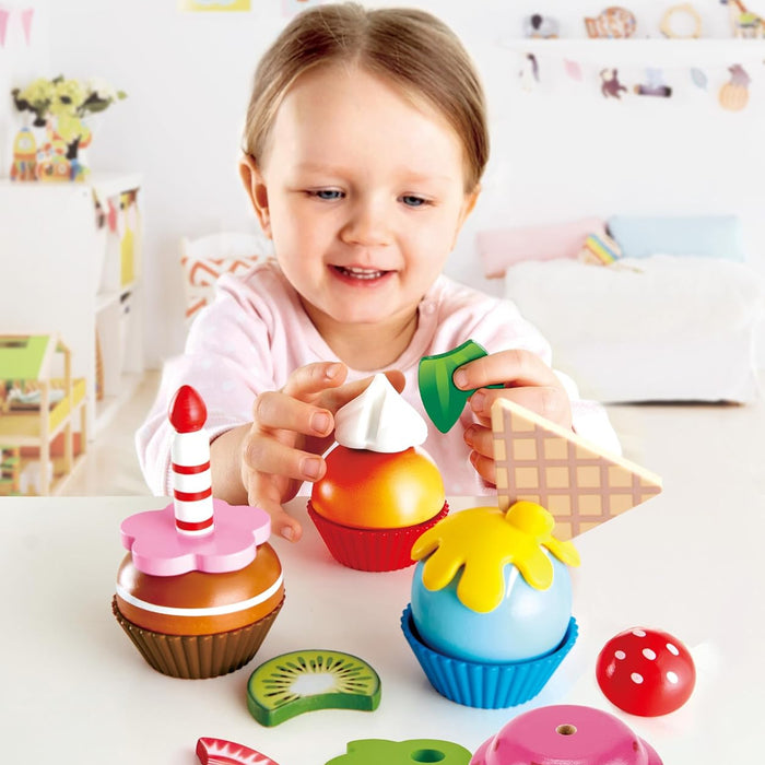 Child playing with colorful toy cupcakes and fruits on a white surface.