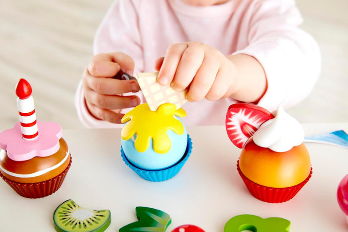 Child playing with colorful toy fruits and a cupcake on a light surface