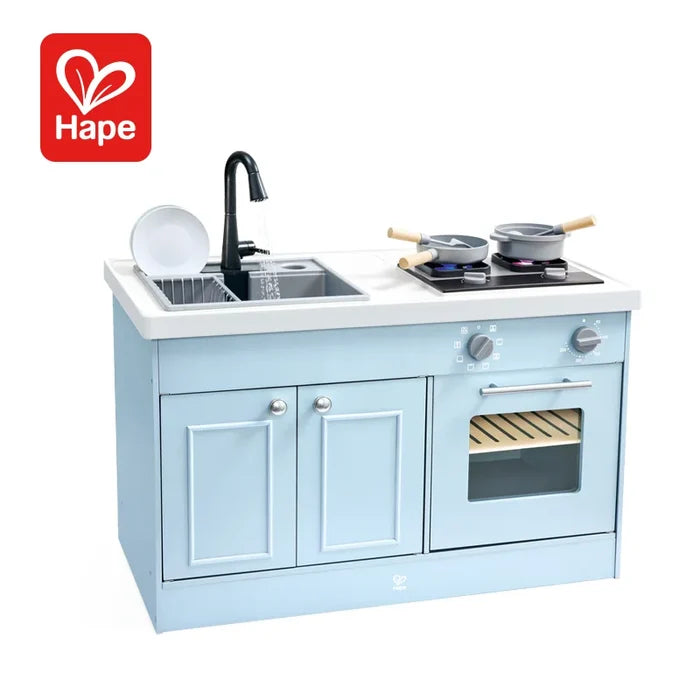 Hape brand children's play kitchen toy in light blue, featuring a double sink with a black faucet, a black stovetop with toy pots, and cabinet doors with silver knobs, shown on a white background.