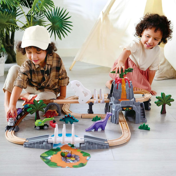 Two children playing with a toy dinosaur track set on a wooden floor.