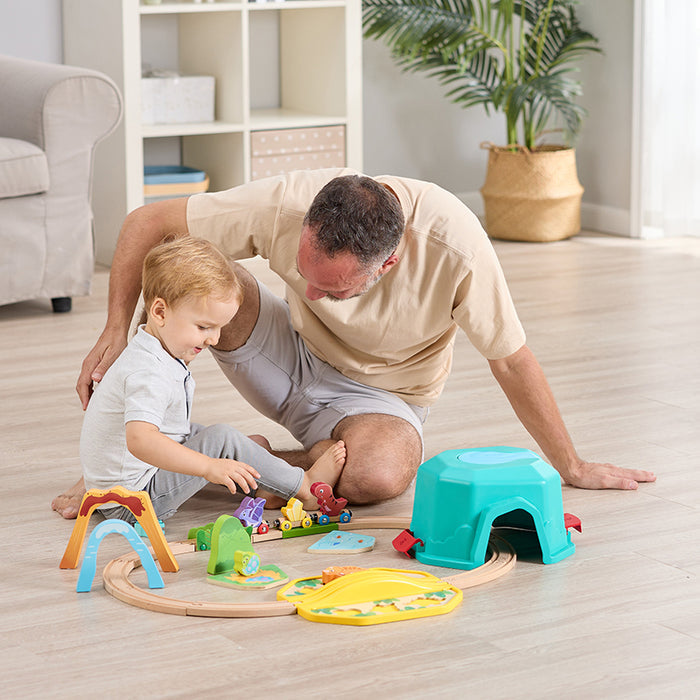 Little boy and man sitting on the floor in a living room playing with the dino train set
