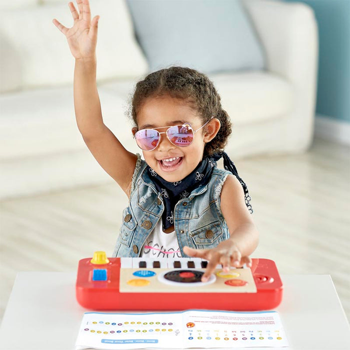 A young child playing with a red portable DJ studio toy with various buttons and sliders.