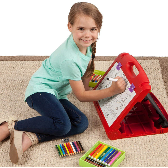 Young girl sitting on a carpeted floor drawing on the Travel Easel