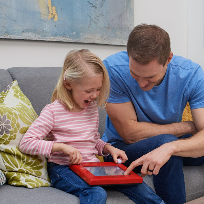 Parent with child playing with Etch-A-Sketch in a living room setting