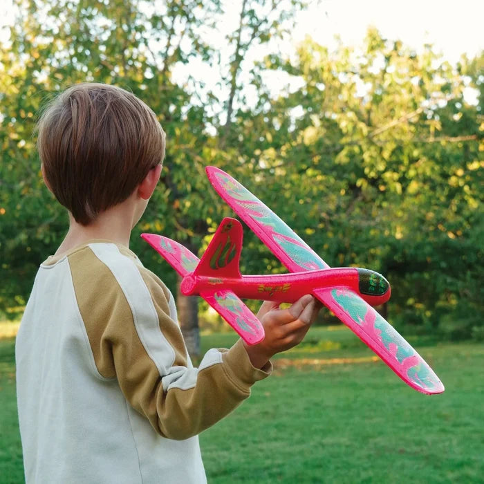 Child holding a red and green toy airplane in a park