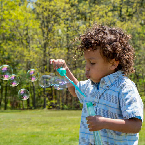 Child blowing bubbles outdoors with trees in the background