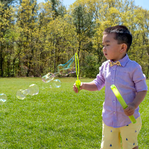 Child blowing bubbles in a grassy field with trees in the background