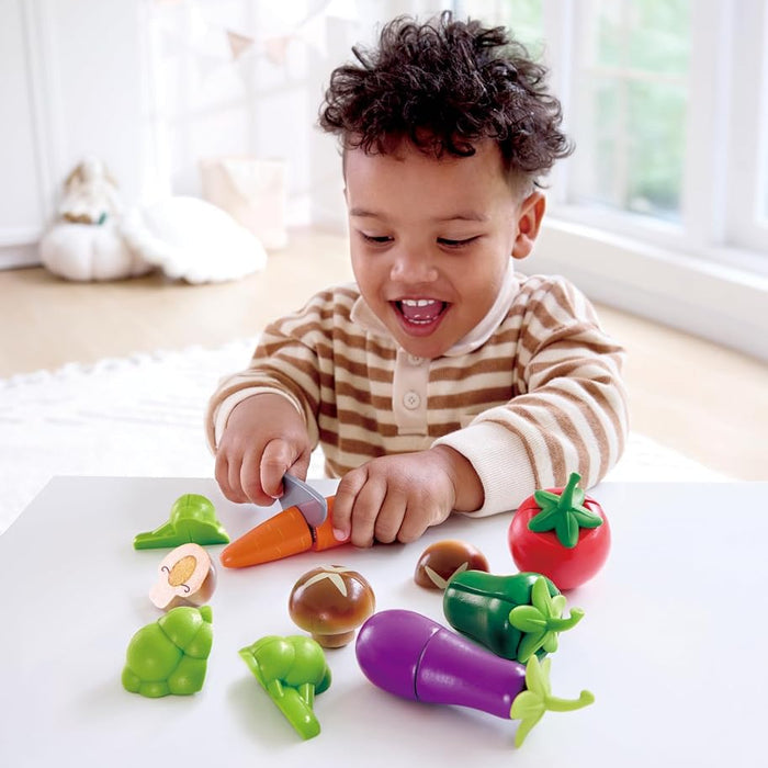 Child playing with toy vegetables on a white surface