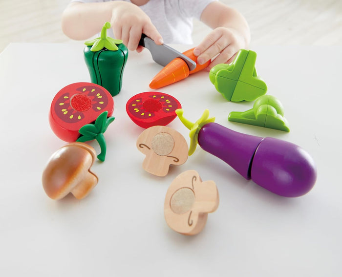 Colorful toy vegetables and on a white surface with a child's hands interacting with them.