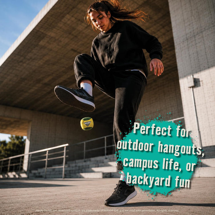A woman in a black sweatshirt and black joggers kicks a yellow Hacky Sack while outdoors under a concrete bridge. The text overlay reads 'Perfect for outdoor hangouts, campus life, or backyard fun'.