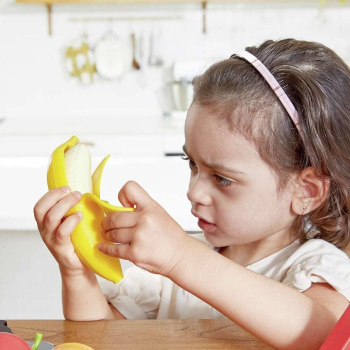 Child peeling a pretend banana in a white kitchen