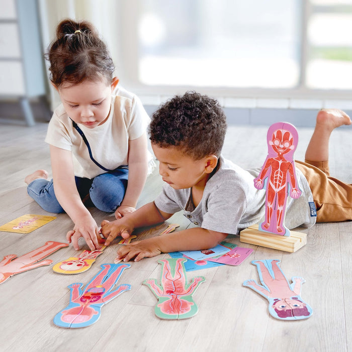 Two children playing with educational body part models on a wooden floor.