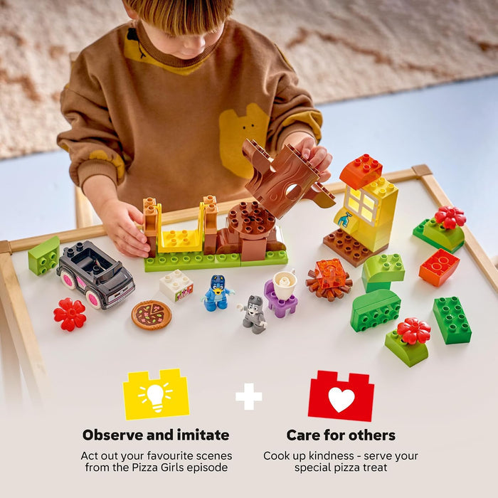 A child wearing a brown sweatshirt plays with a colorful wooden building block toy set on a white table. The set includes various shaped blocks, small toy figures, a pizza piece, and a car.