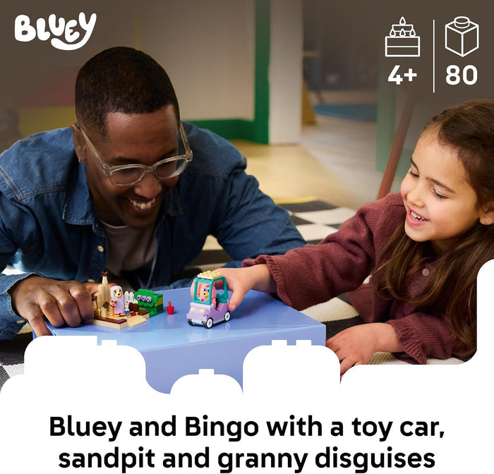 Man and young girl playing with toys, including a toy car and sandpit, in a casual indoor setting.