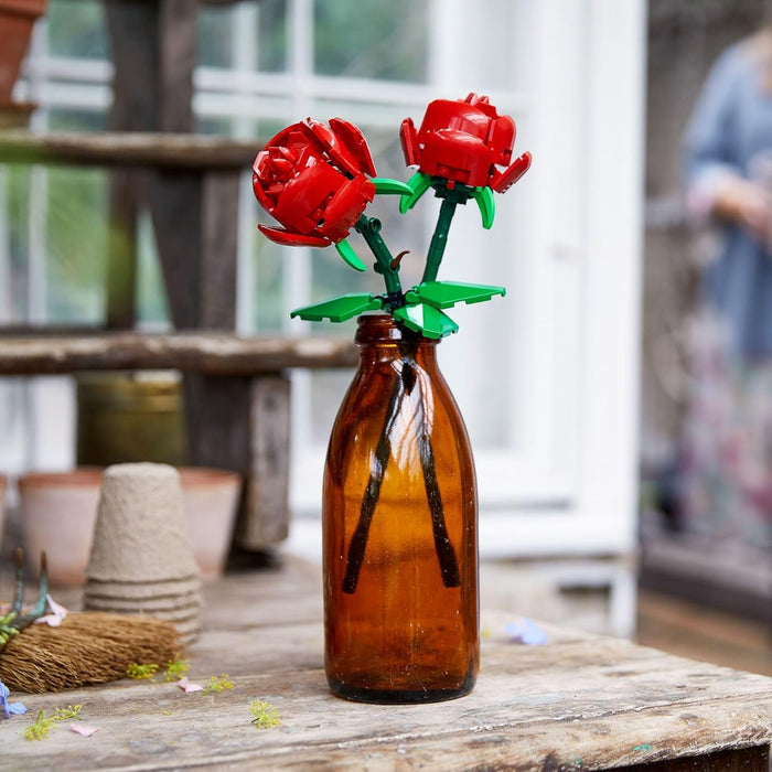Red glass flowers in an amber bottle on a wooden surface with a blurred background