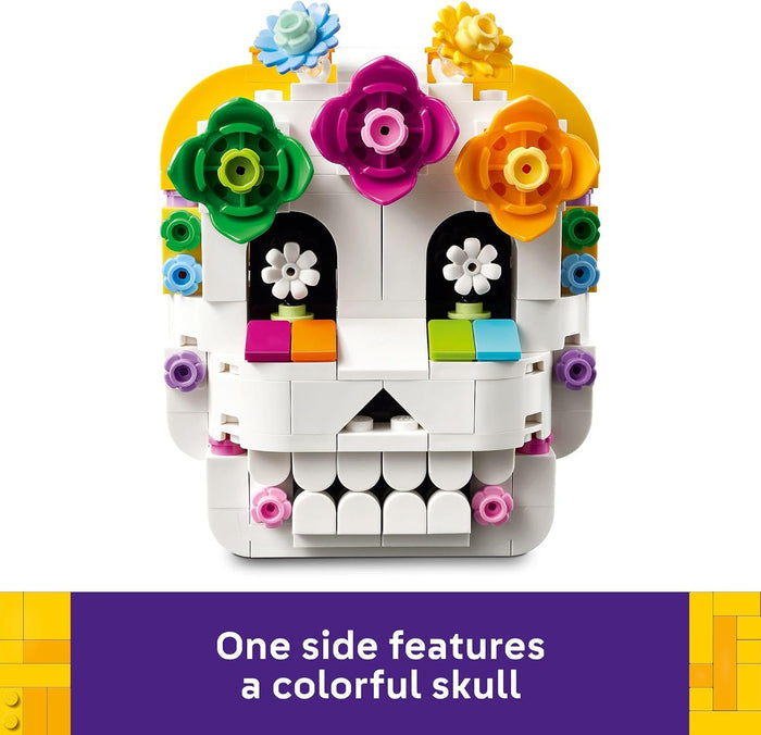 A white LEGO-style sugar skull toy with colorful floral decorations on a white background, plus a purple text banner at the bottom that reads, 'One side features a colorful skull.'.
