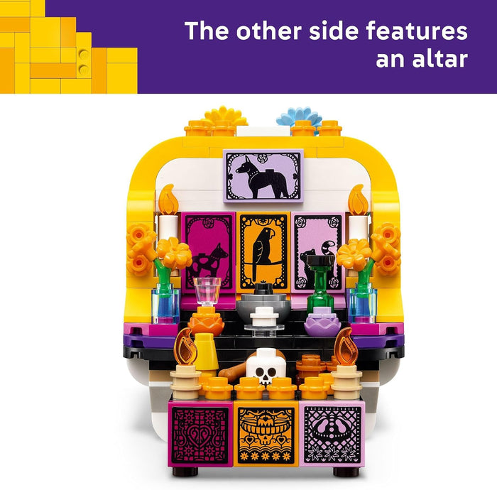 A LEGO-style Day of the Dead altar building set shown on a white background with a purple text banner at the top reading 'The other side features an altar.' The set includes a yellow and white altar structure with purple, black, orange, and pink decorative panels, flowers, candles, and small skeleton details.