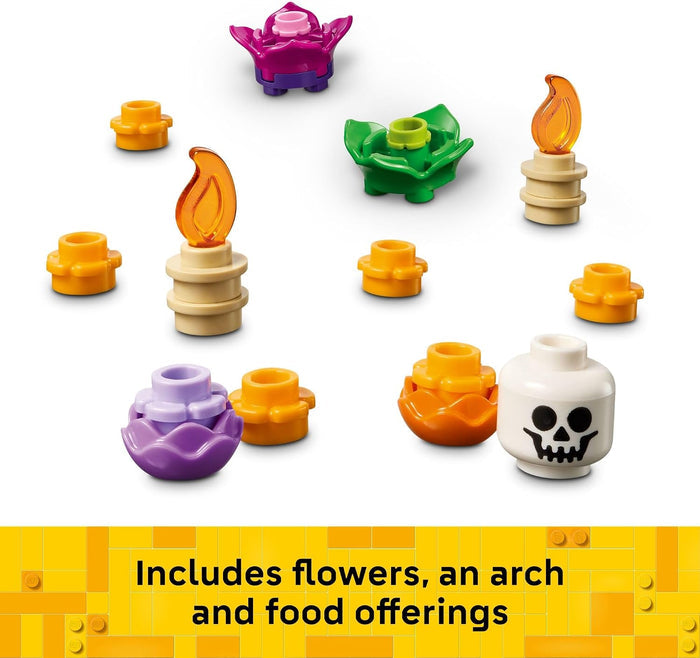 A set of small toy building-block style accessories arranged on a white background, including purple and green flowers, orange candle flames, yellow cup-like pieces, a white skull-faced vessel, and a yellow banner at the bottom with text reading 'Includes flowers, an arch and food offerings.' No person, animal, or real environment is present, so this is Product/Packaging rather than Lifestyle.