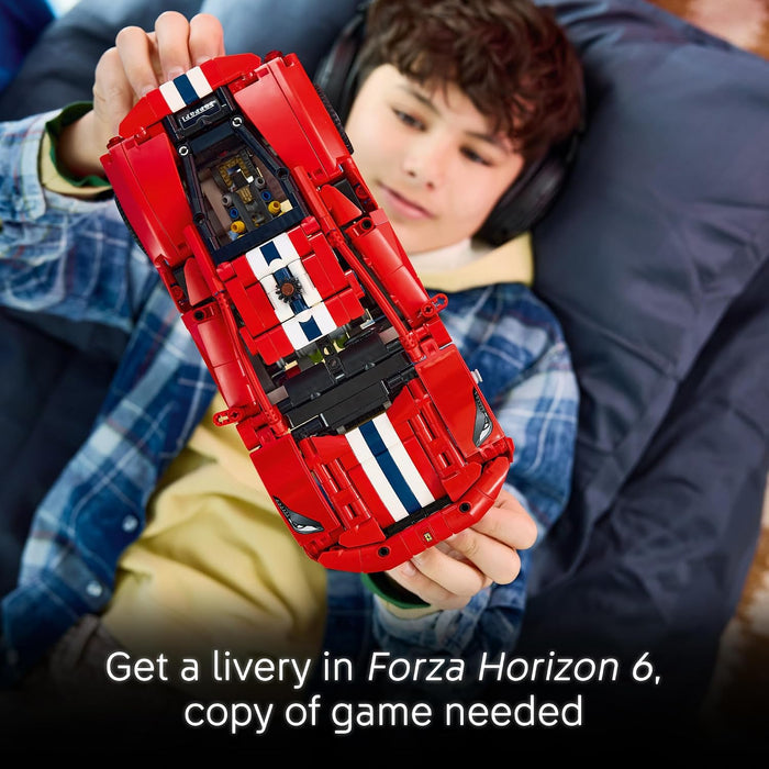 A child holds a red LEGO Forza Horizon 6 toy car with white and blue racing stripes. The child is wearing a blue plaid shirt and headphones, lying on a dark blue cushion.