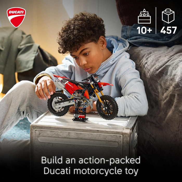 A child sits on a couch holding a red and black LEGO-style Ducati motorcycle toy over a small table. The image includes the Ducati logo, age/feature icons ('10+' and '457'), and the text 'Build an action-packed Ducati motorcycle toy.